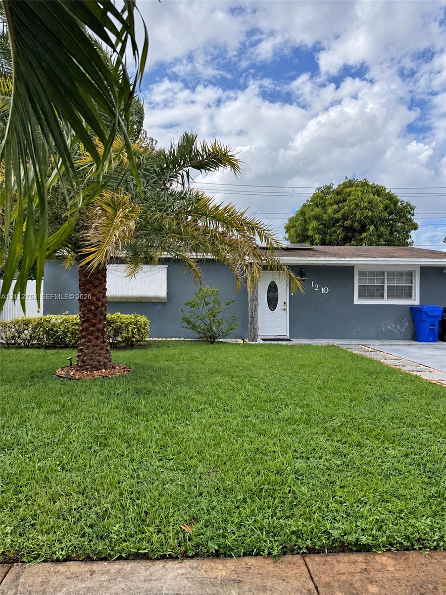 Single-story exterior featuring a gray stucco facade, white entry door with oval glass insert, multi-pane windows, and a mature palm tree on the front lawn
