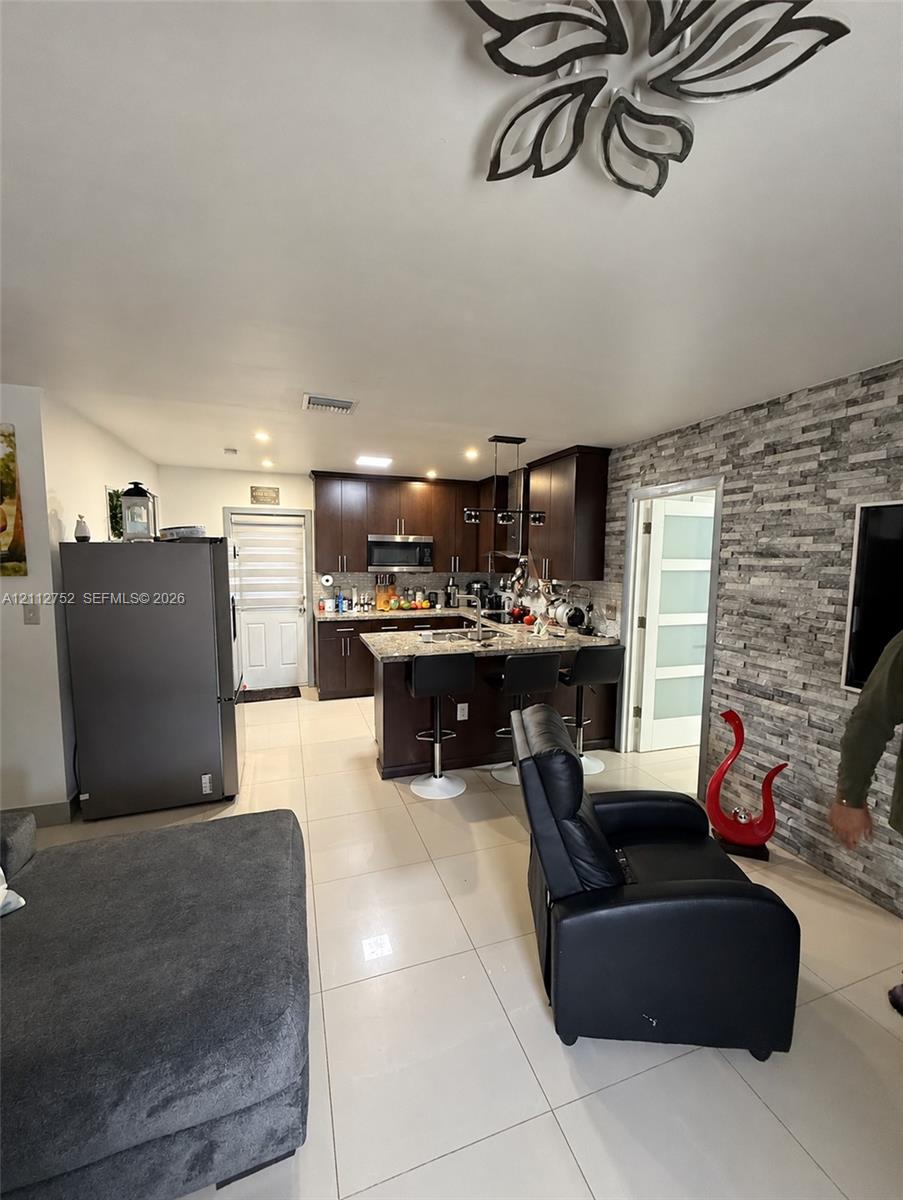 Kitchen featuring dark wood cabinetry, stone-finish countertops, stainless steel appliances, stacked-stone accent wall, and porcelain tile flooring