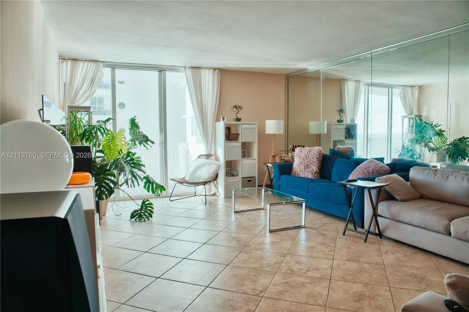 Living area featuring large-format ceramic tile flooring, floor-to-ceiling glass sliding doors, and a full-length mirrored wall