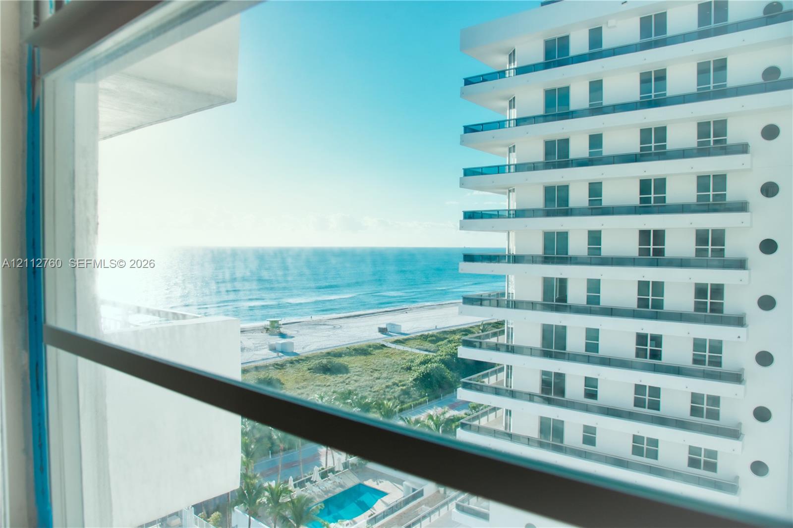 Multi-story white facade high-rise featuring stacked balconies with glass railings, an outdoor swimming pool, and coastal proximity