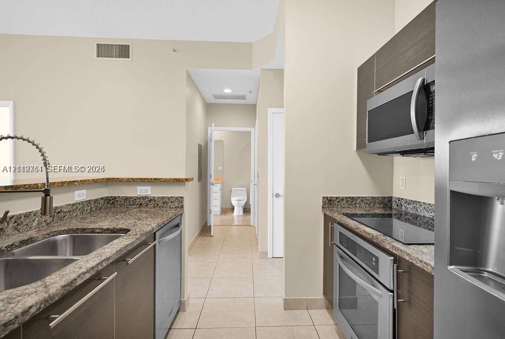 Kitchen featuring dark wood-finish cabinetry, granite countertops, tile flooring, and stainless steel appliances including a built-in microwave, range, and dishwasher