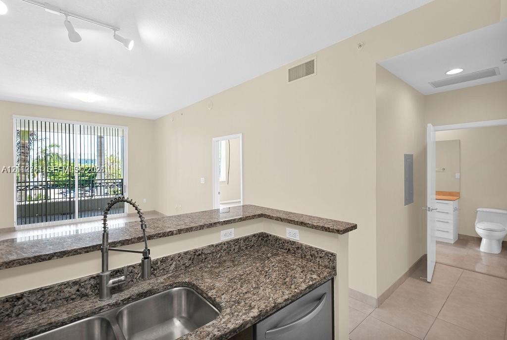 Kitchen featuring a stone-surface breakfast bar, stainless steel double-basin sink, high-arc pull-down faucet, and tiled flooring
