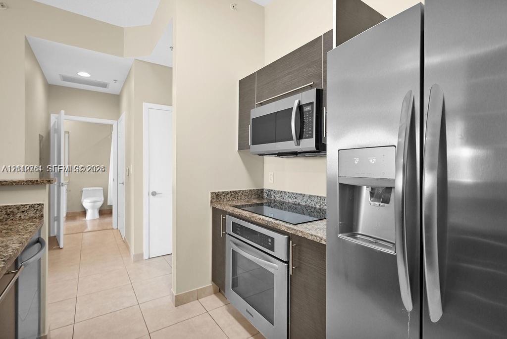 Kitchen featuring dark-toned flat-panel cabinetry, stone countertops, stainless steel appliances, and tile flooring