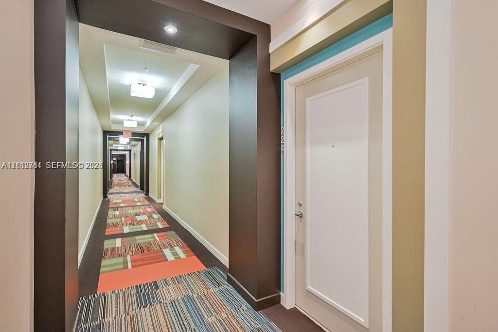 Interior corridor featuring recessed ceiling lighting, multi-tonal patterned carpeting, and recessed door entryways framed by dark accent walls