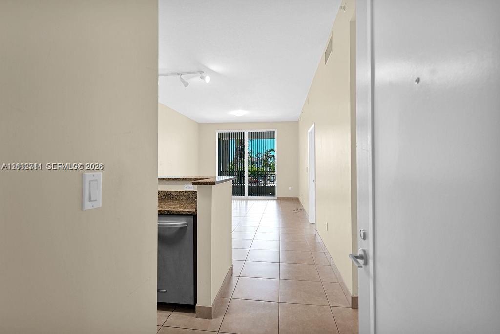 Interior featuring ceramic tile flooring, stone-finish countertops, stainless steel dishwasher, track lighting, and sliding glass doors