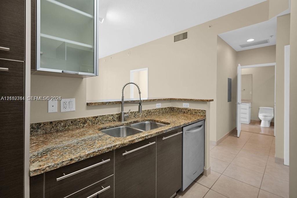 Kitchen featuring dark wood-finish cabinetry, stone-surface countertops, dual-basin stainless steel sink with high-arc faucet, and stainless steel dishwasher