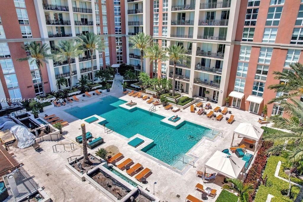 Outdoor swimming pool featuring built-in sun shelves, expansive paved deck, multiple cabanas, and mature palm tree landscaping