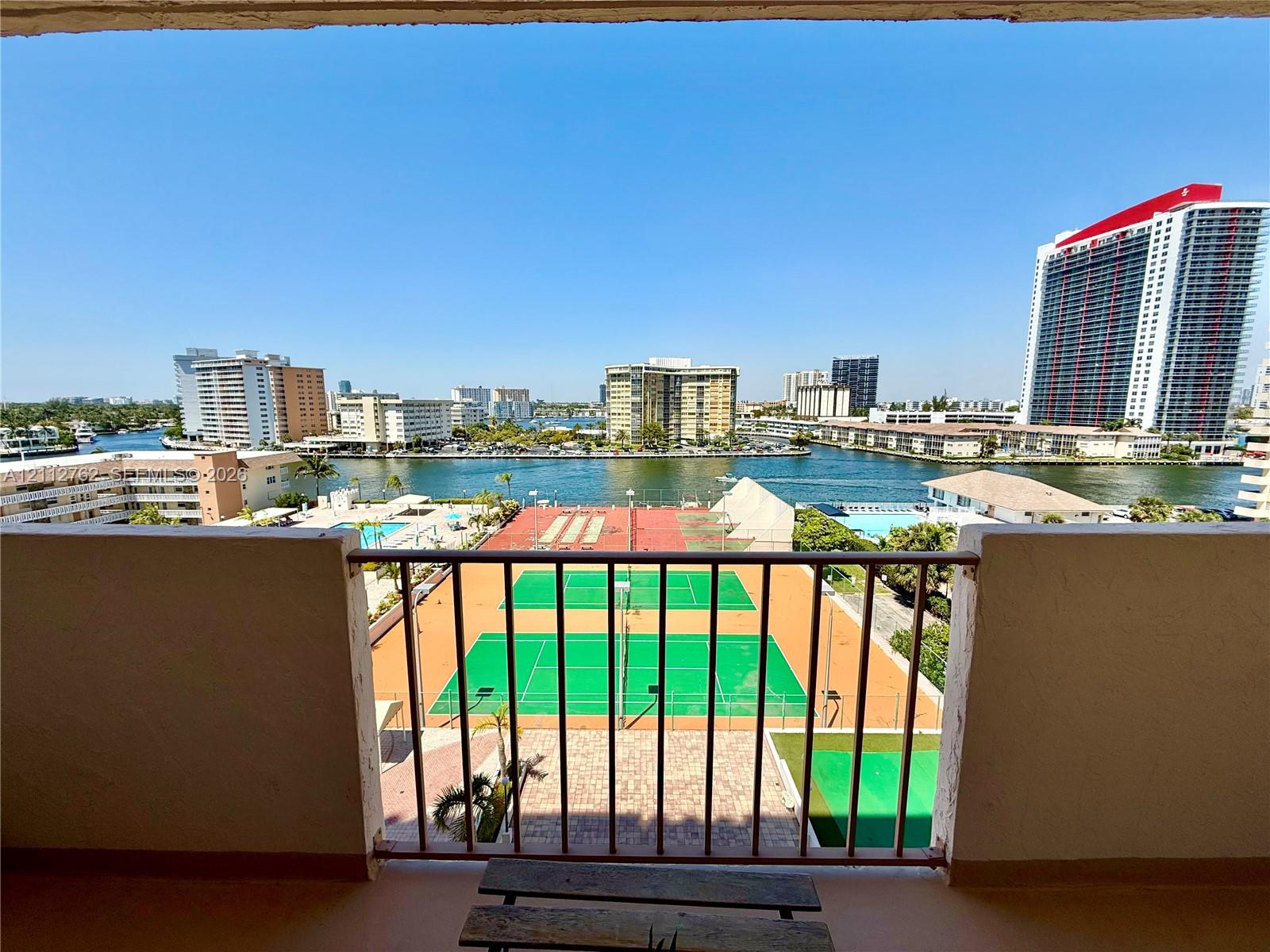 Private balcony featuring a metal railing, overlooking dual tennis courts and a waterfront canal