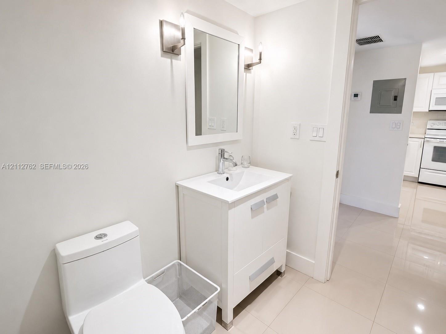 White shaker-style vanity with integrated countertop, rectangular basin, polished chrome faucet, matching framed mirror, and dual wall-mounted light fixtures