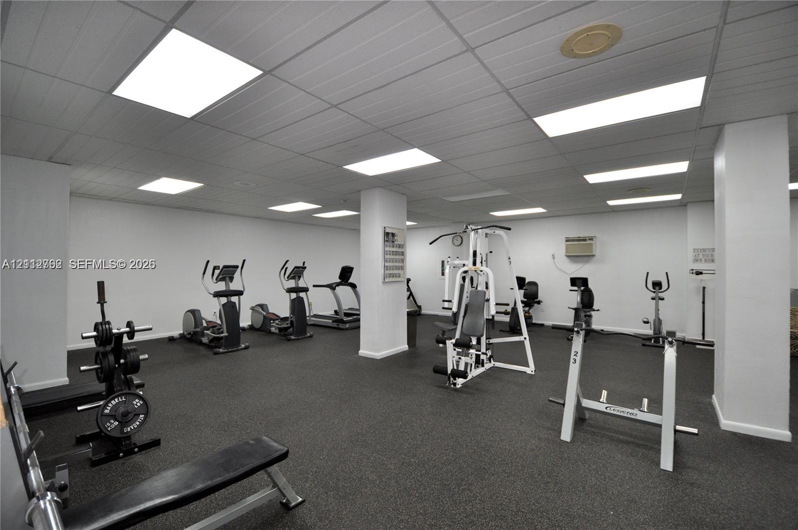 Fitness center featuring a rubberized flooring surface, drop ceiling panels, and integrated recessed lighting