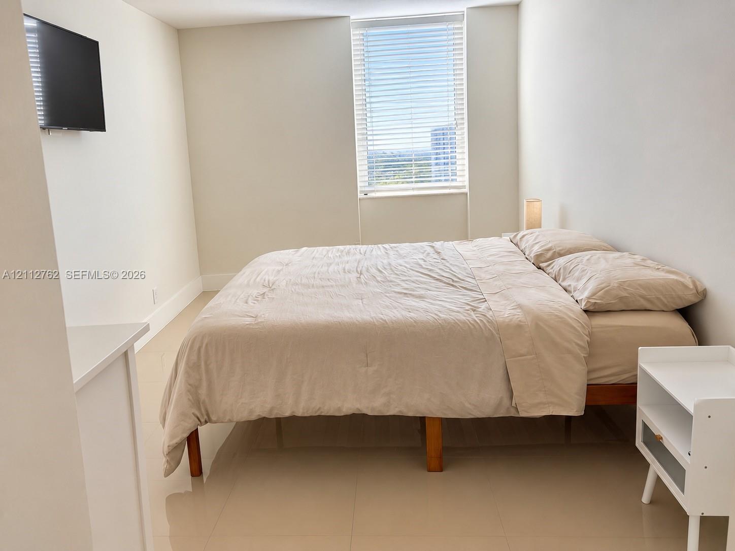 Neutral-toned interior featuring large-format tile flooring, smooth-finish walls, and a tall window equipped with horizontal blinds