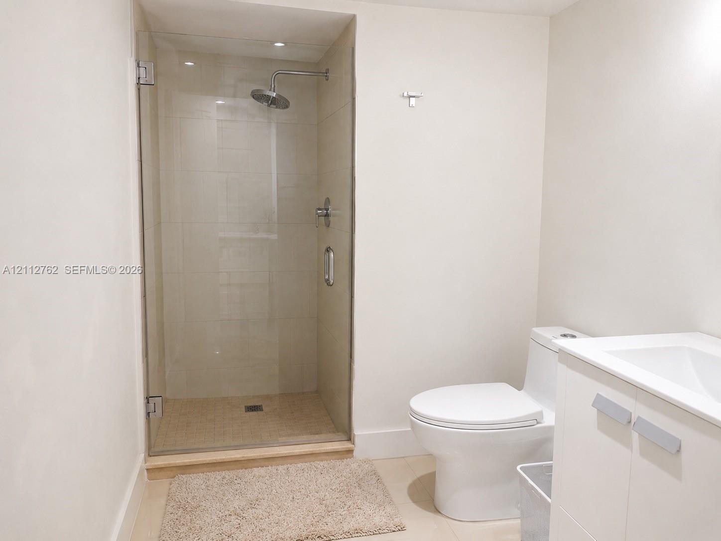 Walk-in shower featuring glass enclosure, wall-mounted rain shower head, light-toned ceramic wall tile, and white vanity with integrated sink