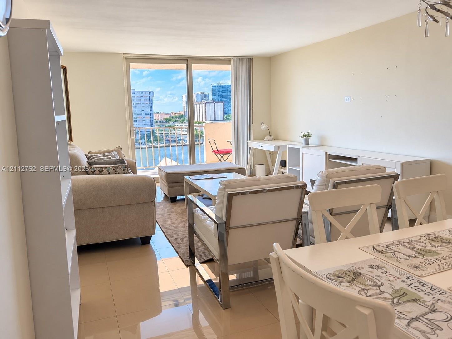 Open-concept living area featuring light-colored tile flooring, floor-to-ceiling sliding glass doors, and a private balcony