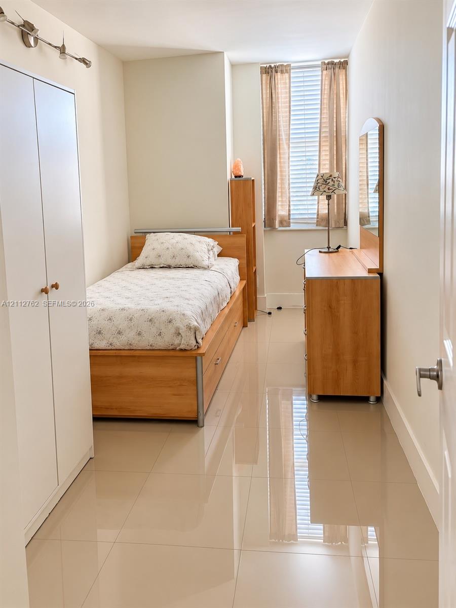 Polished tile flooring, neutral wall finishes, built-in floor-to-ceiling cabinetry, and window with horizontal blinds and drapery hardware