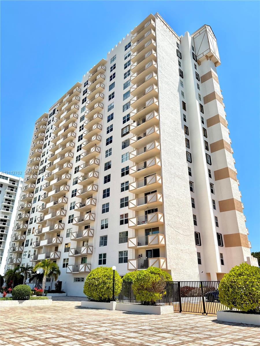 High-rise building exterior featuring tiered balconies with railing accents, masonry facade, and paved ground-level hardscaping