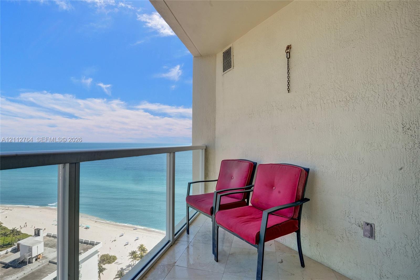 Covered balcony with stone-tile flooring and glass panel railing overlooking the oceanfront