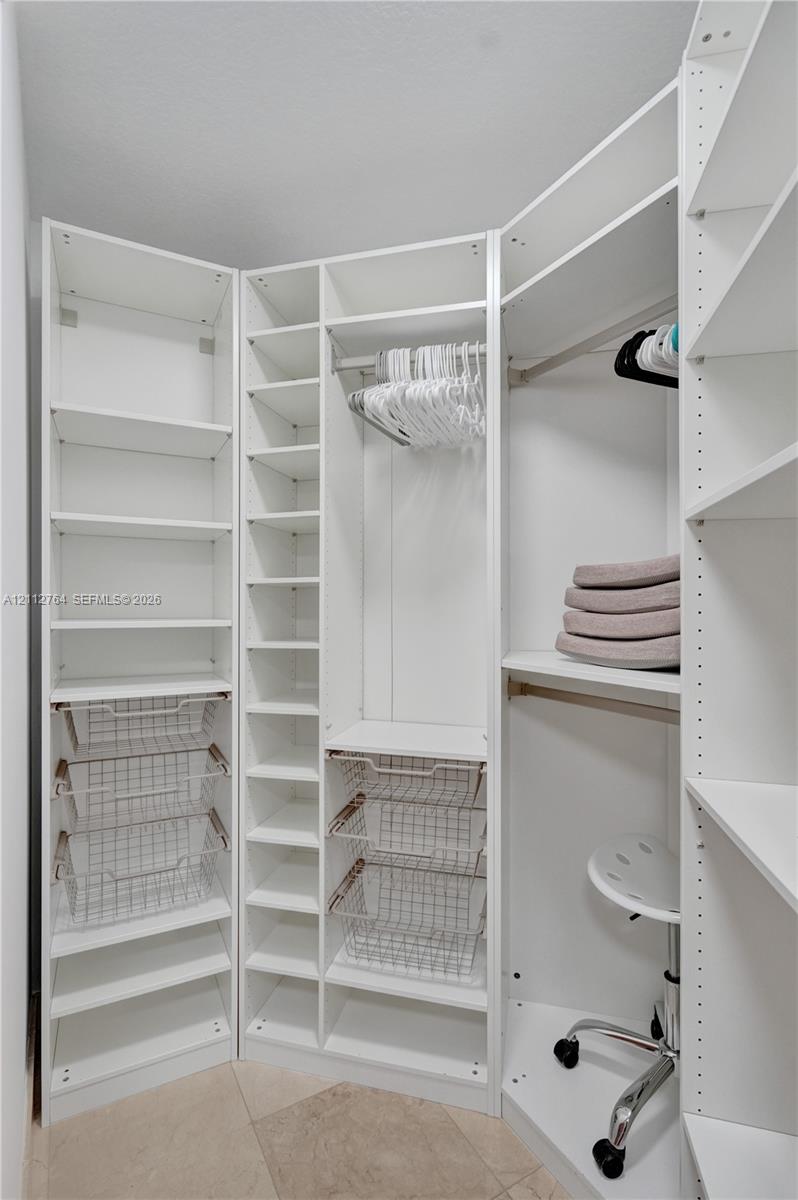 Custom walk-in closet featuring white built-in shelving, adjustable hanging rods, integrated wire storage baskets, and tile flooring