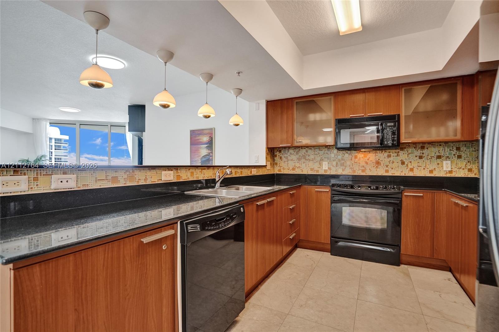 Kitchen featuring natural wood-finish cabinetry, dark solid-surface countertops, multi-toned glass tile backsplash, tile flooring, and four pendant lights