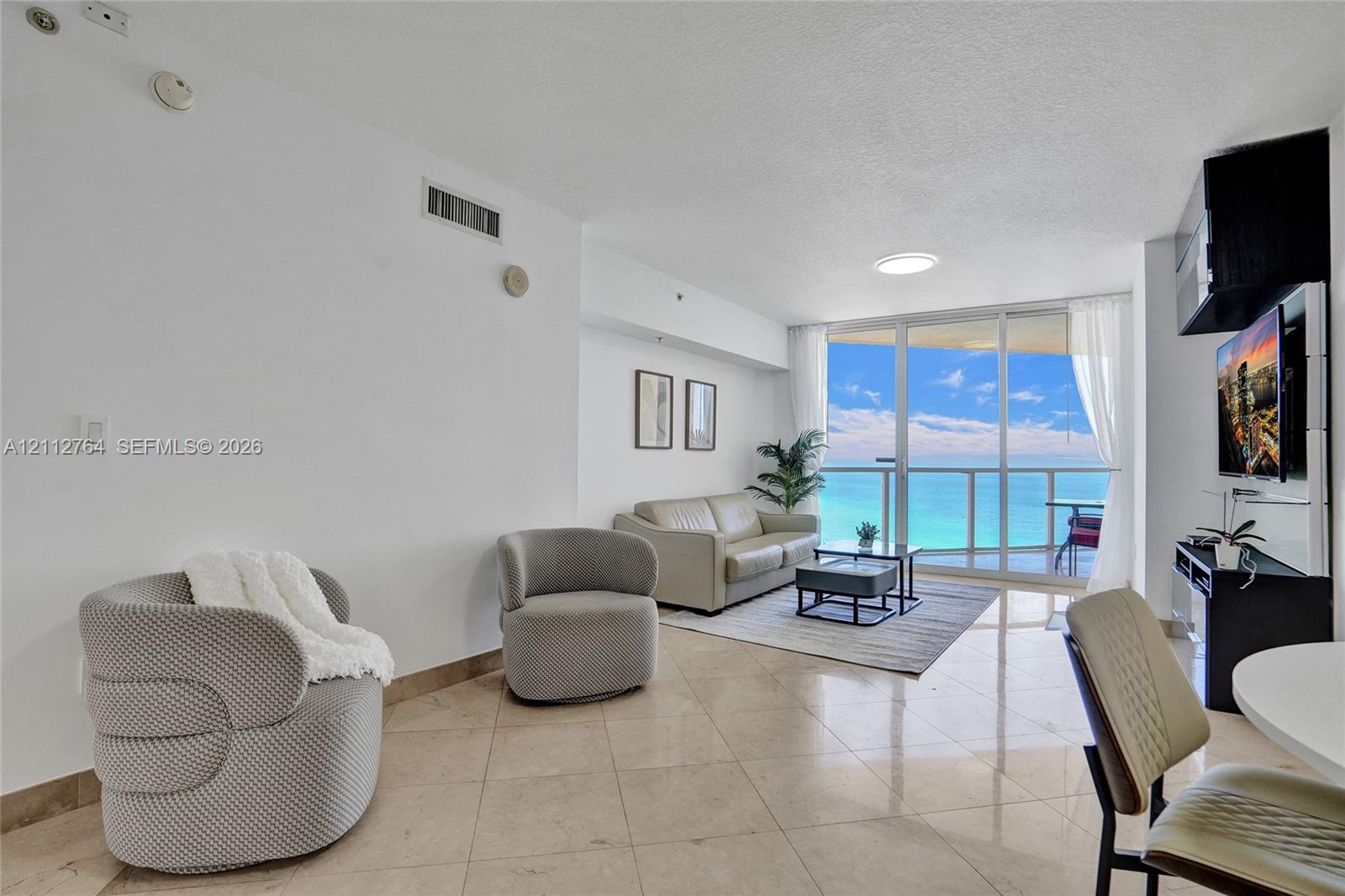 Living space featuring polished stone tile flooring, floor-to-ceiling glass paneling, and access to a private balcony