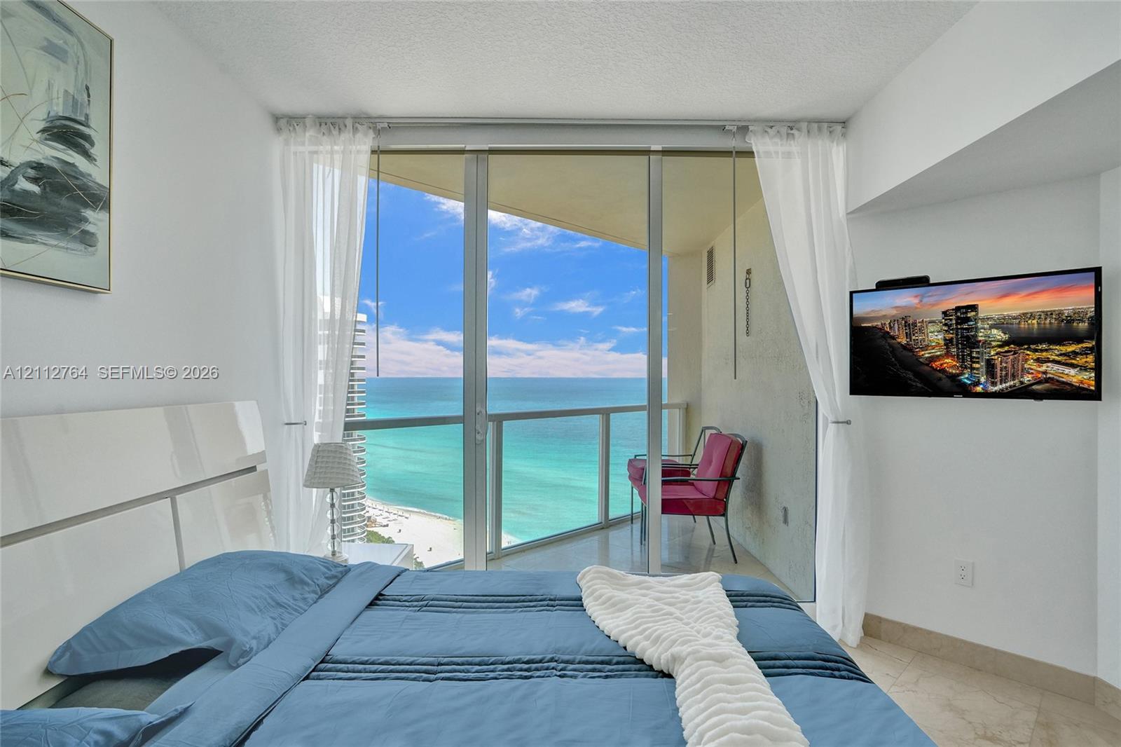 Floor-to-ceiling glass sliding doors opening to an exterior balcony with a glass railing, complemented by expansive ocean scenery