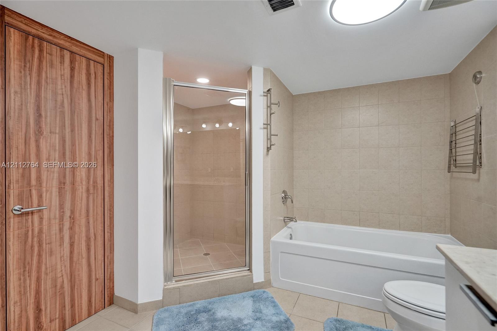 Bathroom featuring a glass-enclosed shower, a deep soaking tub, neutral tile surround, and a wood-finish door