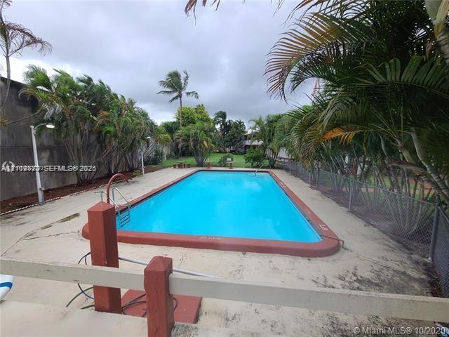 Rectangular in-ground swimming pool featuring a terra cotta border, metal handrail, concrete pool deck, perimeter fencing, and mature palm trees