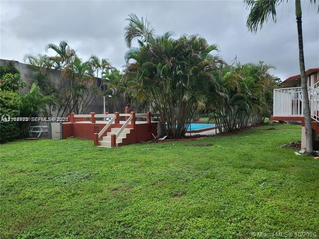 Ground-level pool with a concrete surround, elevated deck featuring white railings, and mature palm trees set within a grass lawn