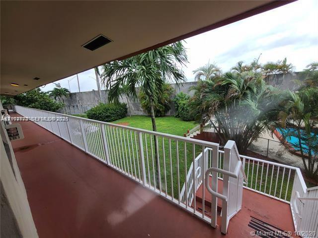 Covered balcony featuring white metal railings, stairs, concrete flooring, exterior lighting, and overlooking a green space with a swimming pool and mature palm trees
