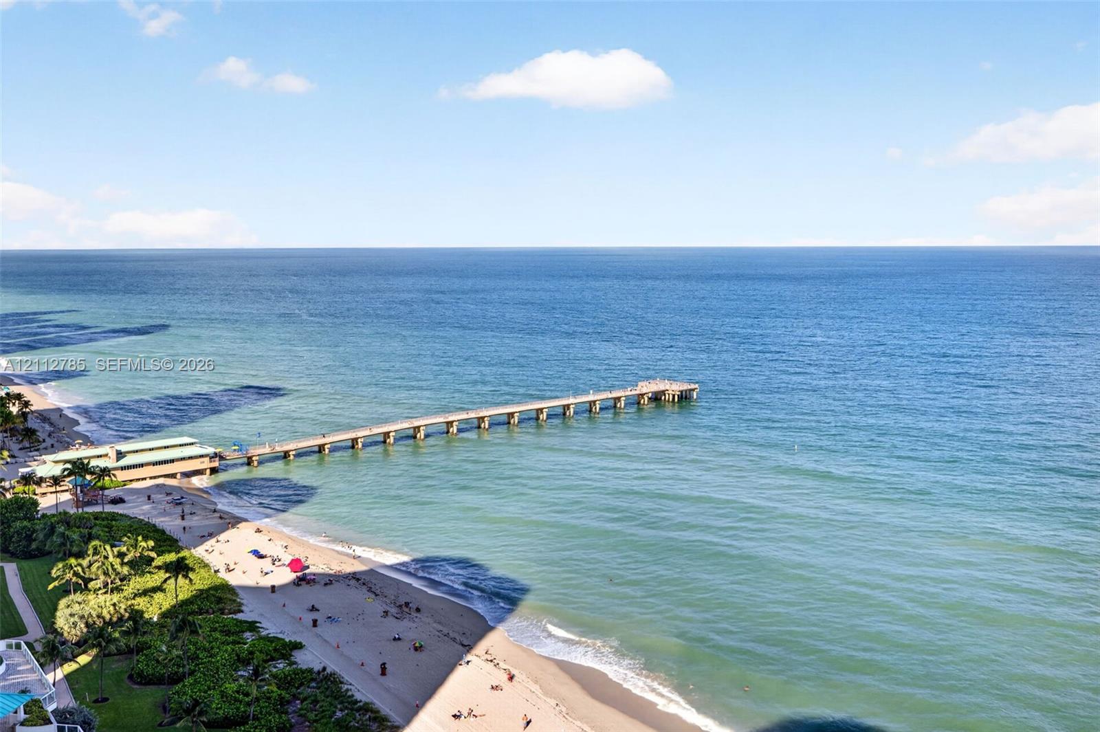 Oceanfront location featuring expansive sandy beach access, a long wooden pier, mature palm trees, and manicured green space