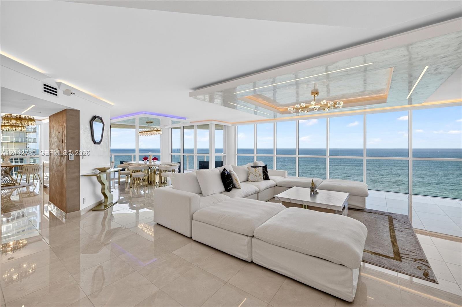 Floor-to-ceiling windows featuring ocean horizon, recessed tray ceiling with integrated lighting, polished stone-finish flooring, and architectural metallic-finish wall paneling Floor-to-ceiling windows featuring ocean horizon, recessed tray ceiling with integrated lighting, polished stone-finish flooring, and architectural metallic-finish wall paneling