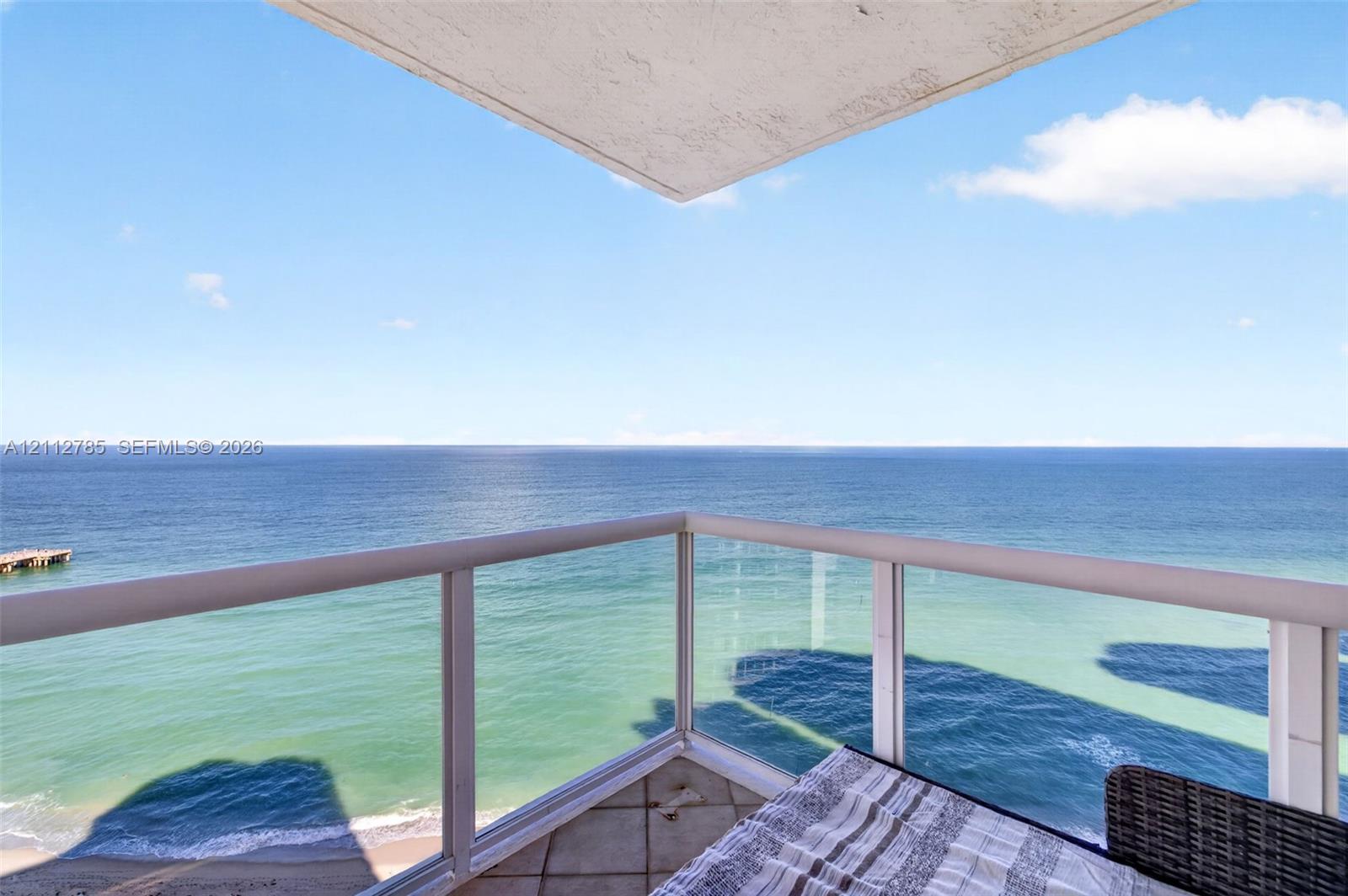 Covered balcony with glass panel railing and tile flooring, featuring an expansive ocean panorama