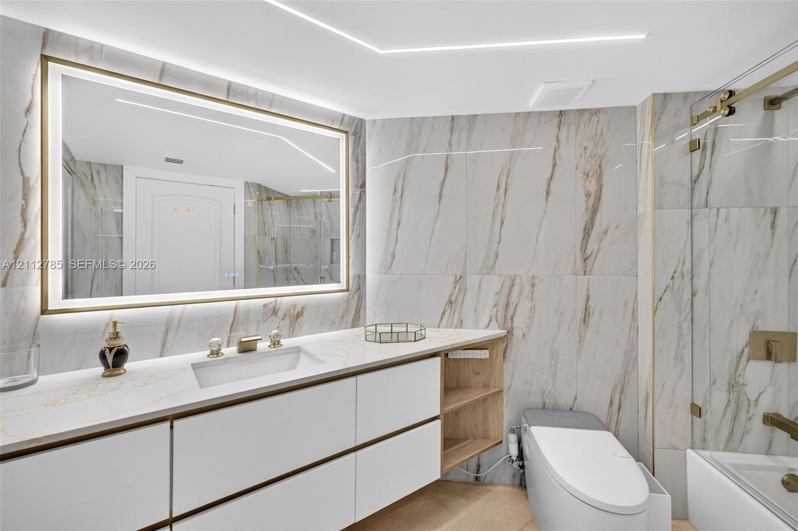 Bathroom featuring large-format stone-finish wall tile, a floating vanity with integrated cabinetry, an illuminated vanity mirror, and a glass-enclosed shower with metallic hardware