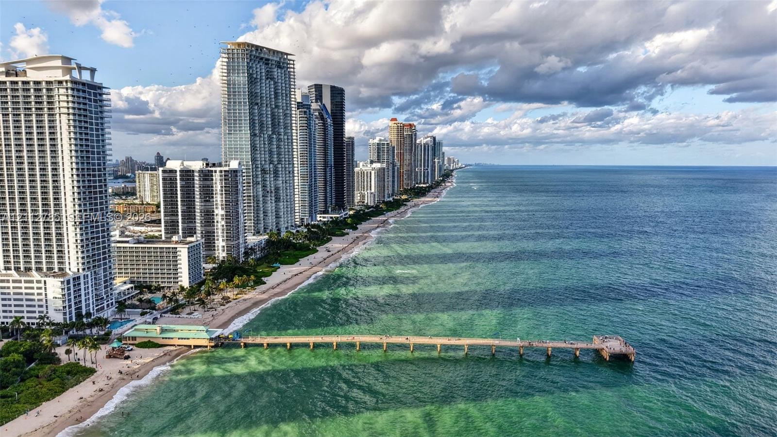 Coastal high-rise buildings situated along a sandy shoreline with direct ocean access and a prominent structural pier