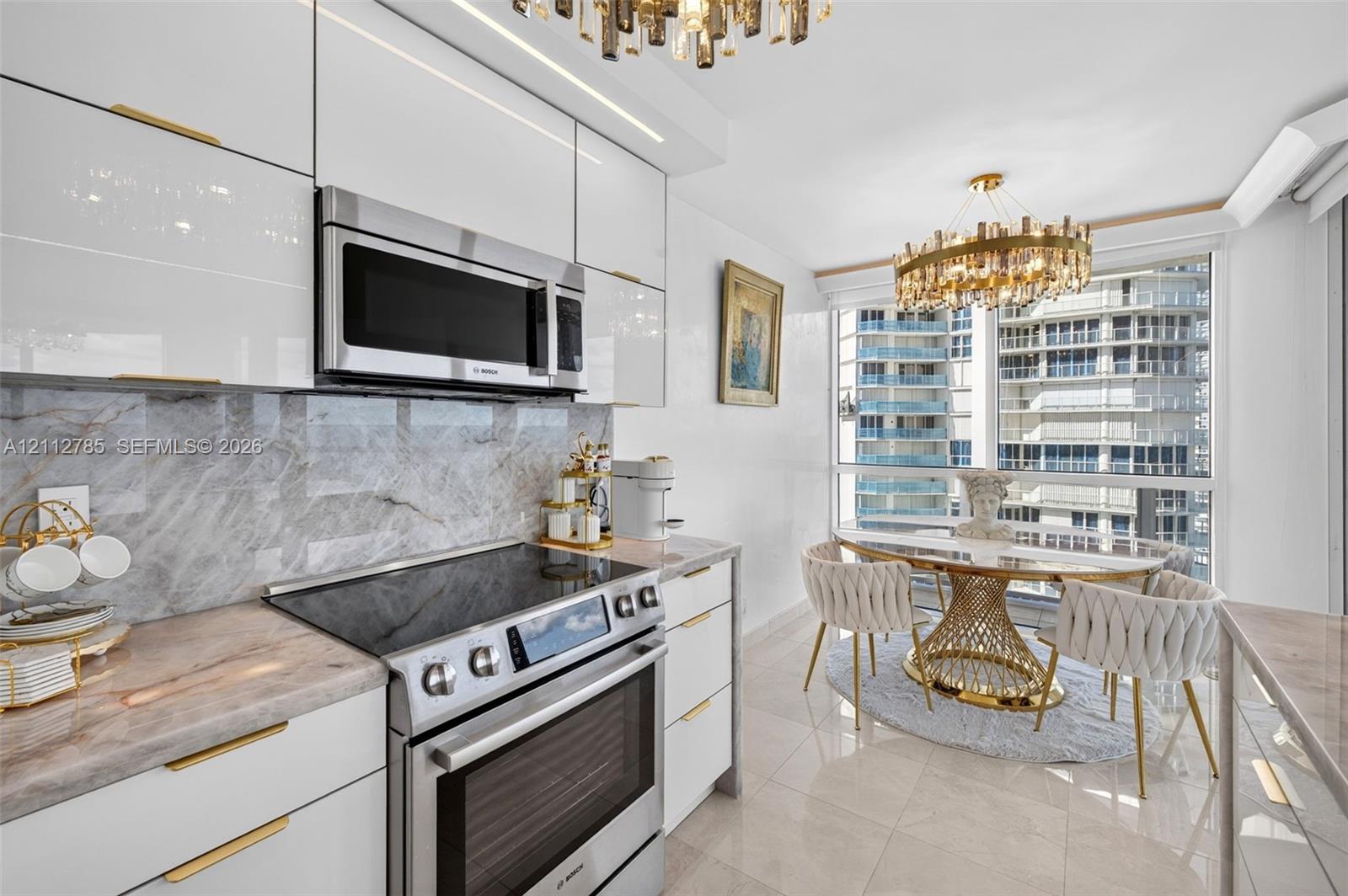 Kitchen featuring high-gloss white cabinetry, gold-tone hardware, stone-surface countertops, stone-tile backsplash, and integrated stainless steel appliances