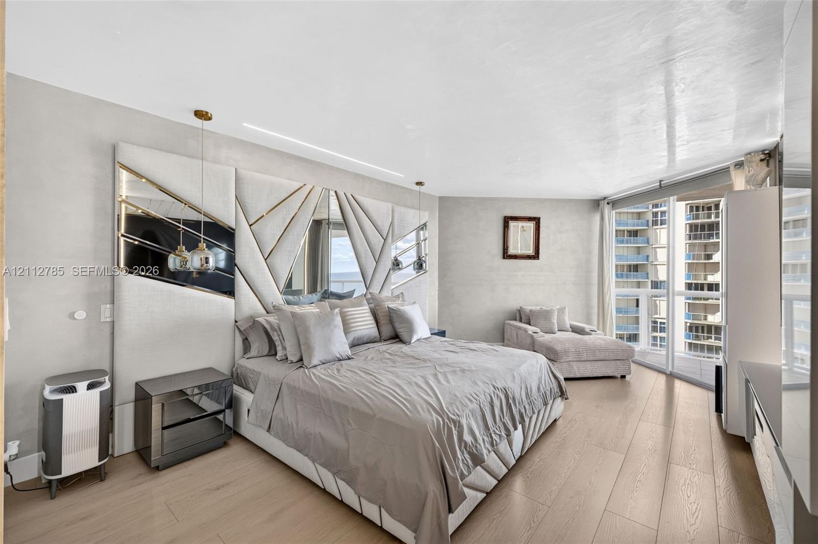 Custom floor-to-ceiling geometric headboard with integrated mirror panels, wood-finish flooring, recessed ceiling lighting, and floor-to-ceiling windows