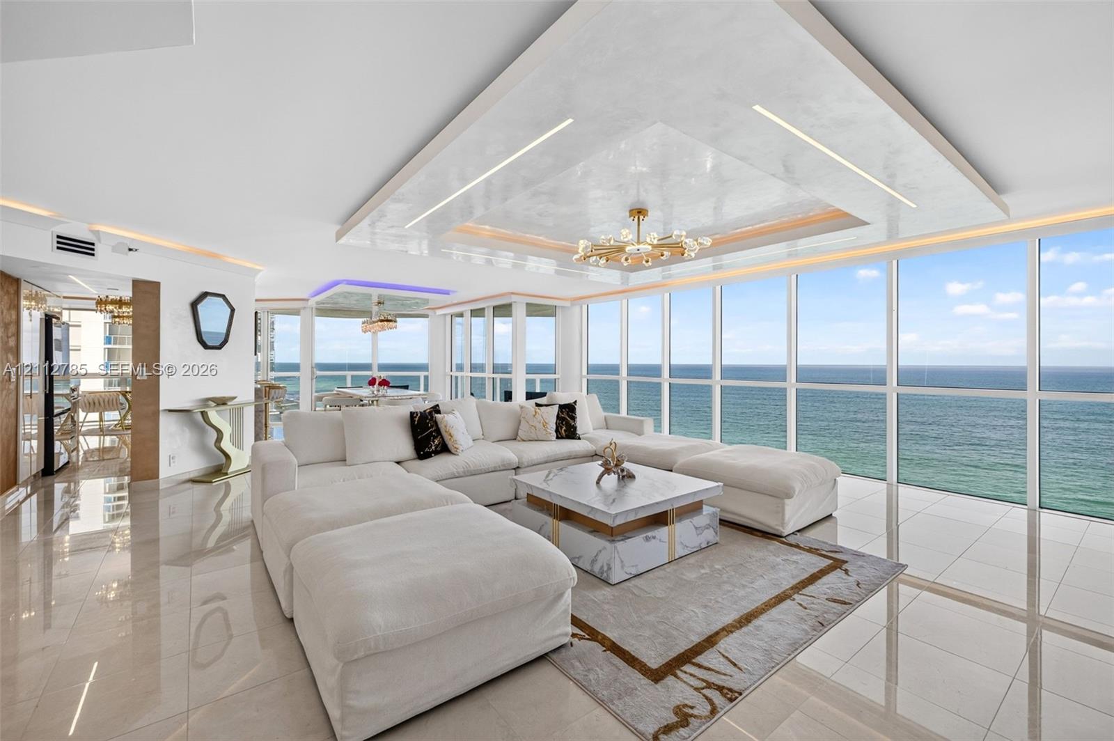 Floor-to-ceiling glass windows, recessed tray ceiling with accent lighting, polished tile flooring, and custom chandelier Floor-to-ceiling glass windows, recessed tray ceiling with accent lighting, polished tile flooring, and custom chandelier
