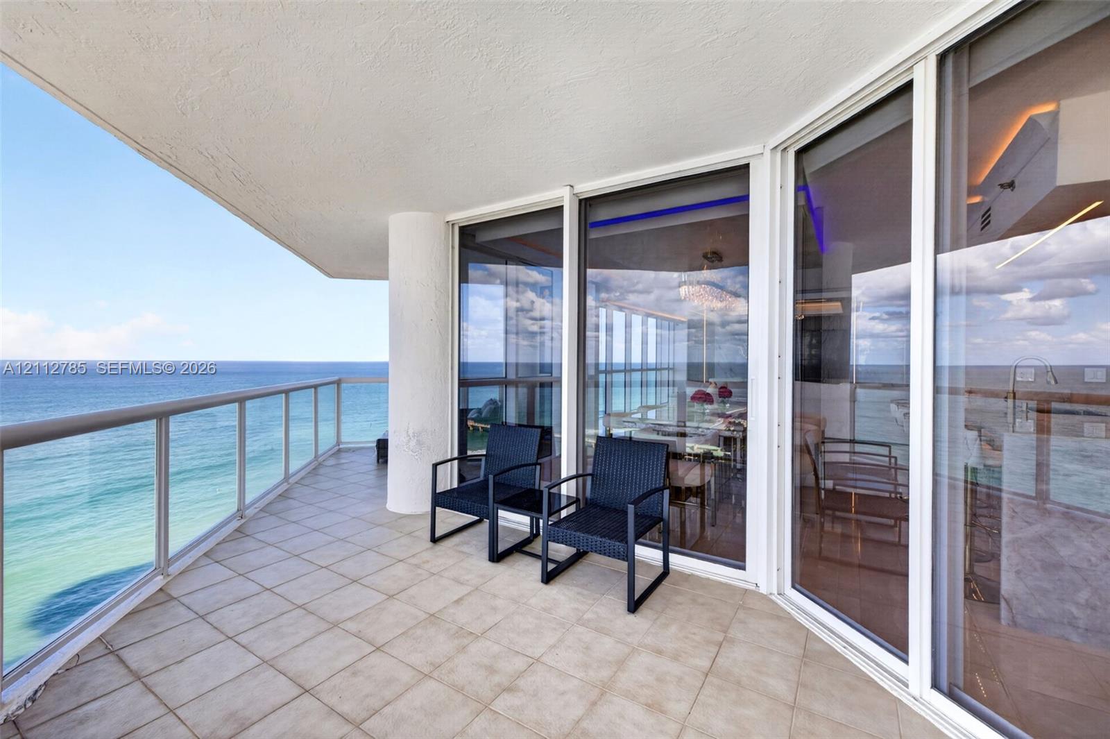 Covered balcony featuring tile flooring, glass panel railing, and expansive floor-to-ceiling sliding glass doors