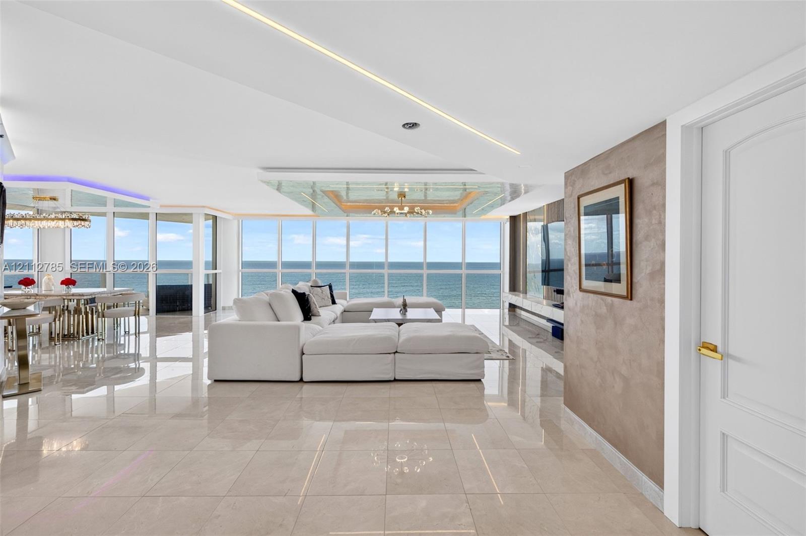 Floor-to-ceiling windows with ocean scenery, polished stone flooring, linear recessed ceiling lighting, and a custom textured accent wall Floor-to-ceiling windows with ocean scenery, polished stone flooring, linear recessed ceiling lighting, and a custom textured accent wall