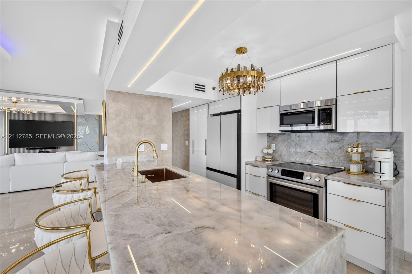 Kitchen featuring high-gloss cabinetry, stone-surface countertops, an integrated island sink with a gold-tone faucet, built-in stainless steel appliances, and a decorative circular chandelier
