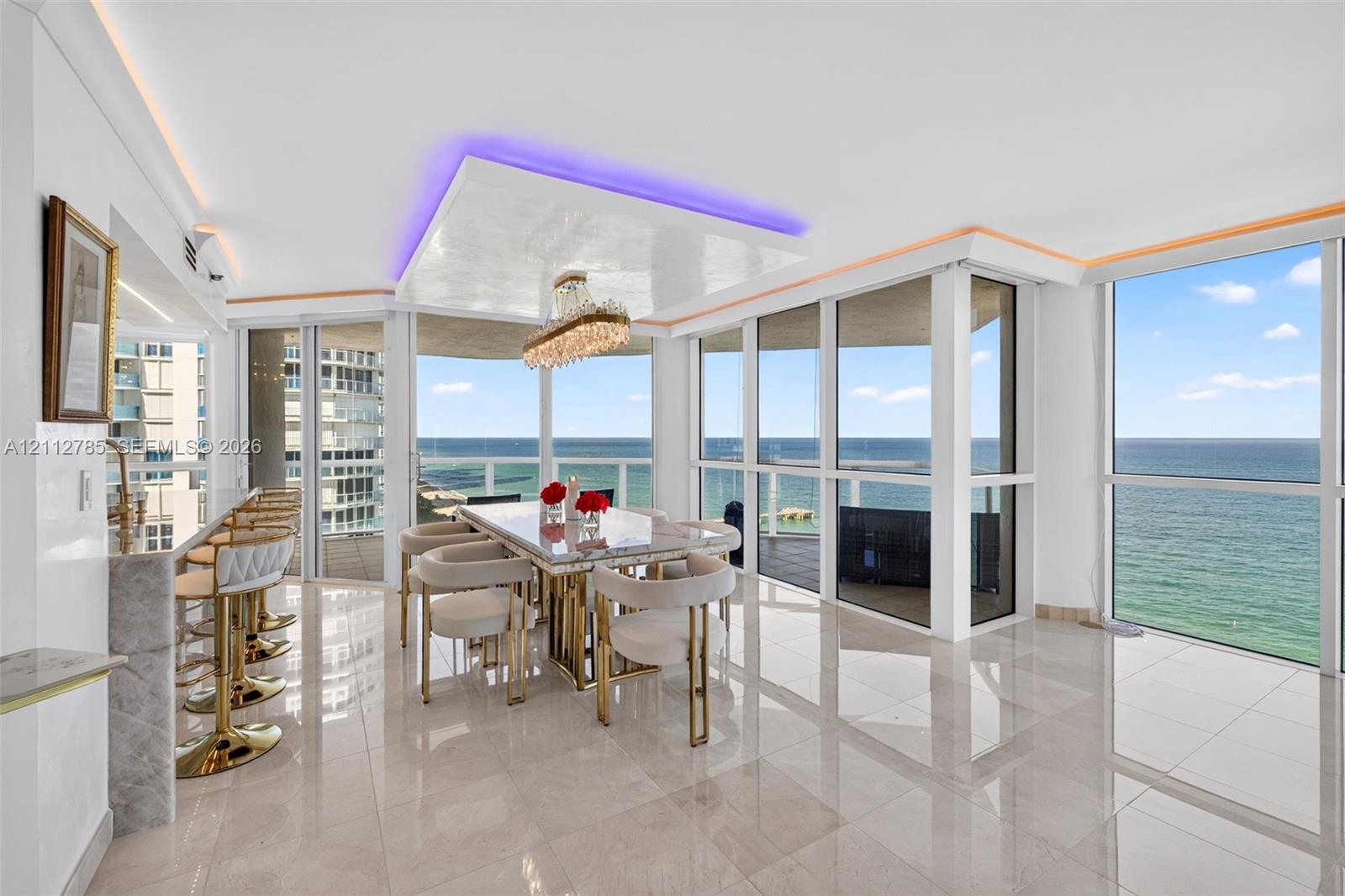 Open-concept area featuring polished stone-finish flooring, floor-to-ceiling glass windows, recessed ceiling lighting with perimeter accent detailing, and an integrated stone-finish breakfast bar