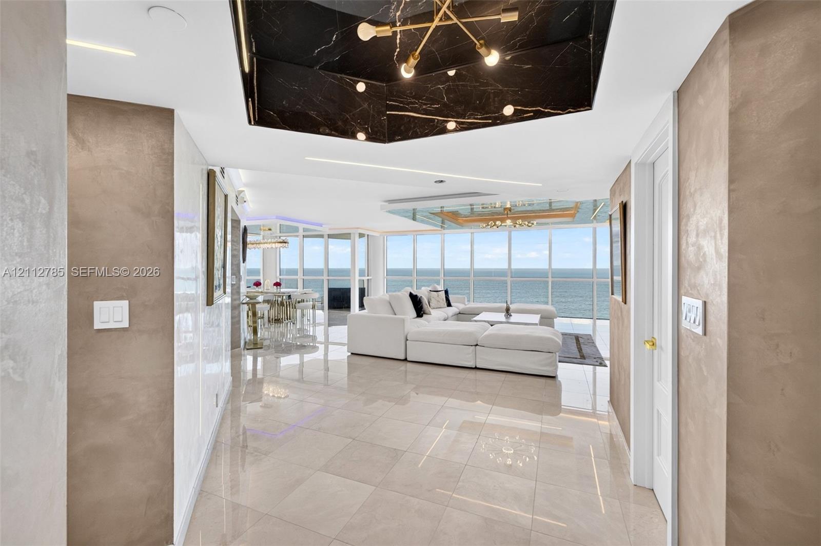 Floor-to-ceiling windows, polished tile flooring, metallic wall finishes, recessed tray ceiling with dark stone cladding, and built-in linear lighting Floor-to-ceiling windows, polished tile flooring, metallic wall finishes, recessed tray ceiling with dark stone cladding, and built-in linear lighting