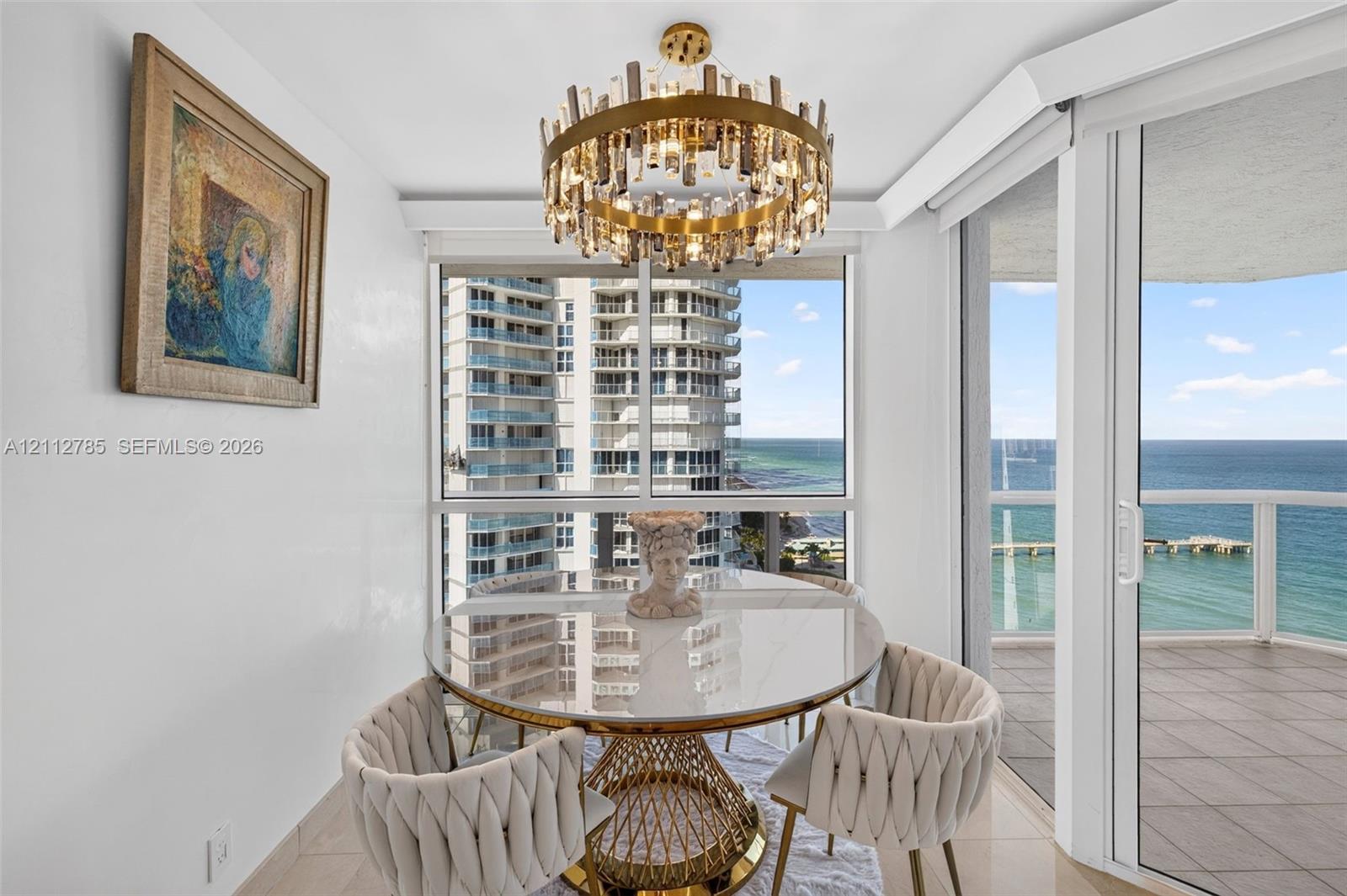 Circular chandelier with tiered crystal detailing, floor-to-ceiling windows, sliding glass door, and tile flooring