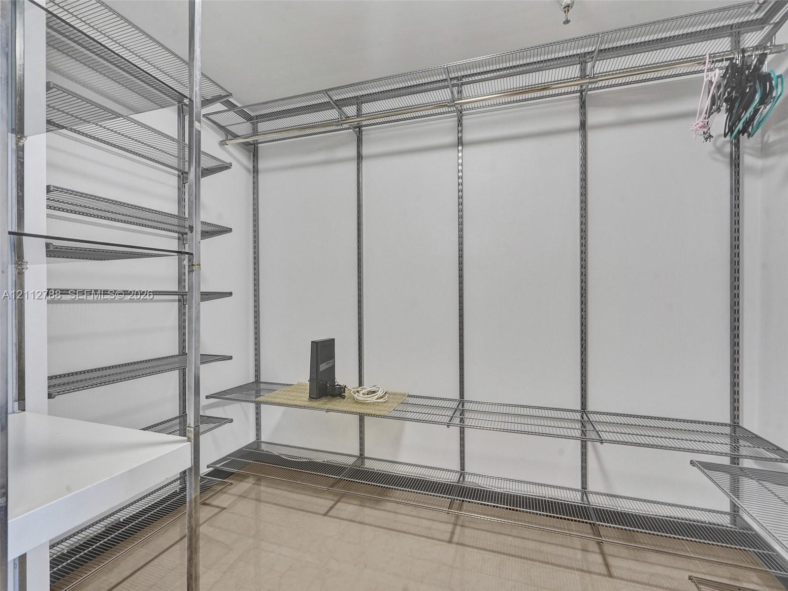 Walk-in storage space featuring adjustable metal wire shelving, integrated hanging rods, and polished tile flooring