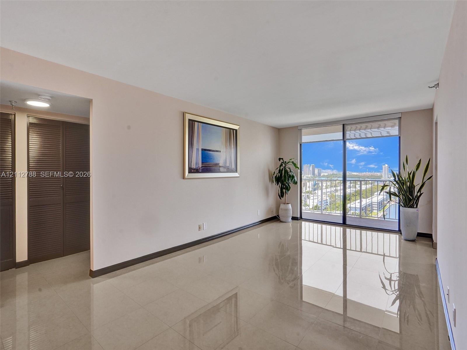 Living area featuring polished tile flooring, floor-to-ceiling glass sliding doors, a metal balcony railing, and built-in louvered closet doors