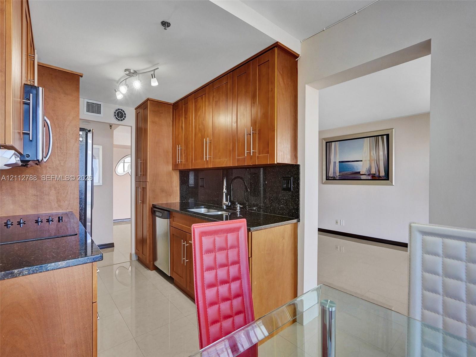 Kitchen featuring natural finish wood cabinetry, dark stone countertops, stainless steel appliances, and tile flooring