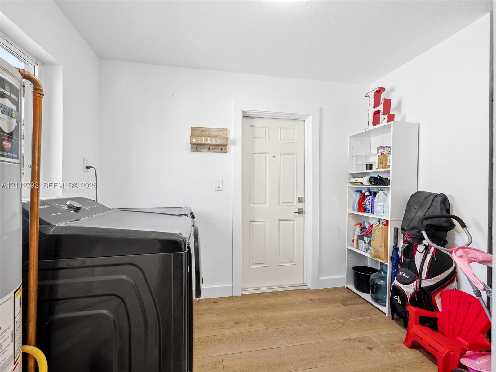 Utility area featuring wood-finish flooring, a six-panel entry door, and white wall finishes