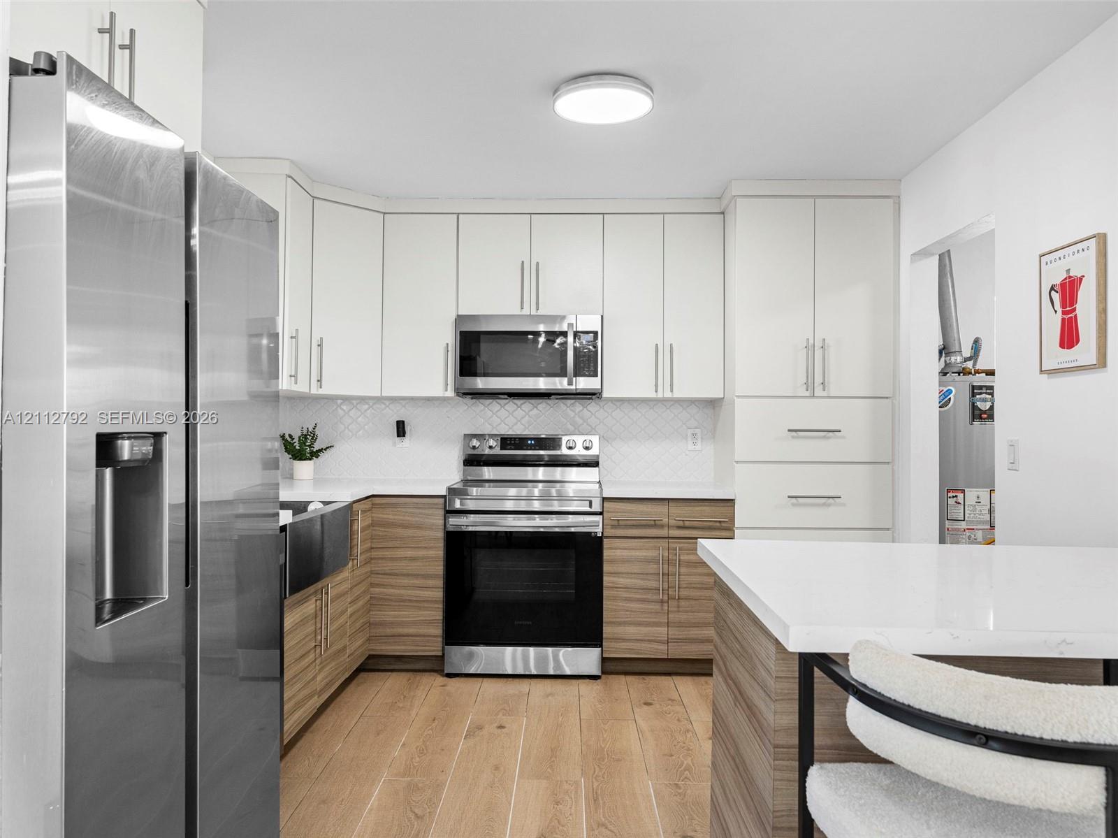 Kitchen featuring two-tone cabinetry with wood-finish lower units, solid-surface countertops, a stainless steel apron-front sink, and a suite of stainless steel appliances