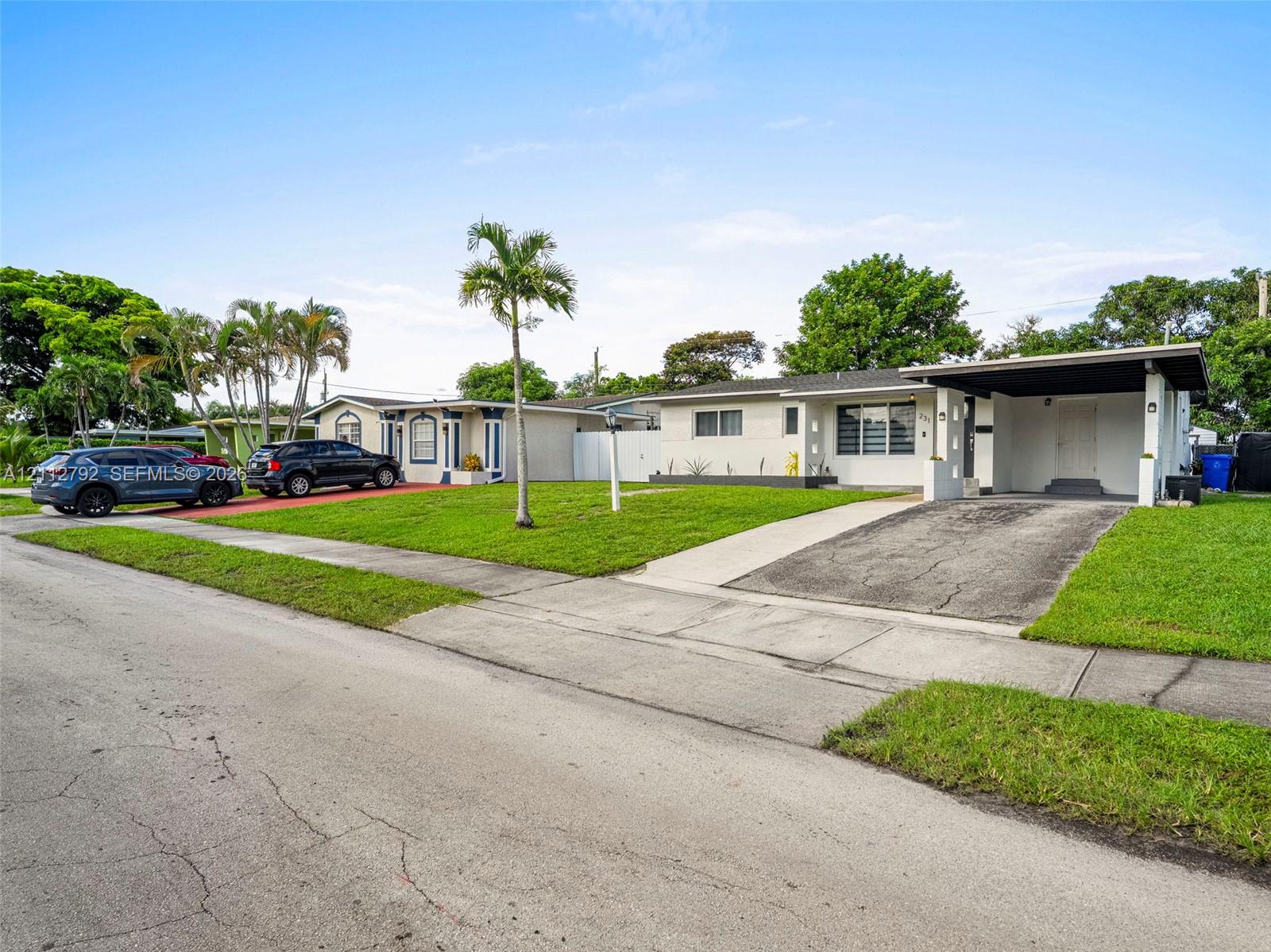 Single-story exterior featuring painted brick masonry, an integrated carport, a concrete driveway, and mature palm landscaping