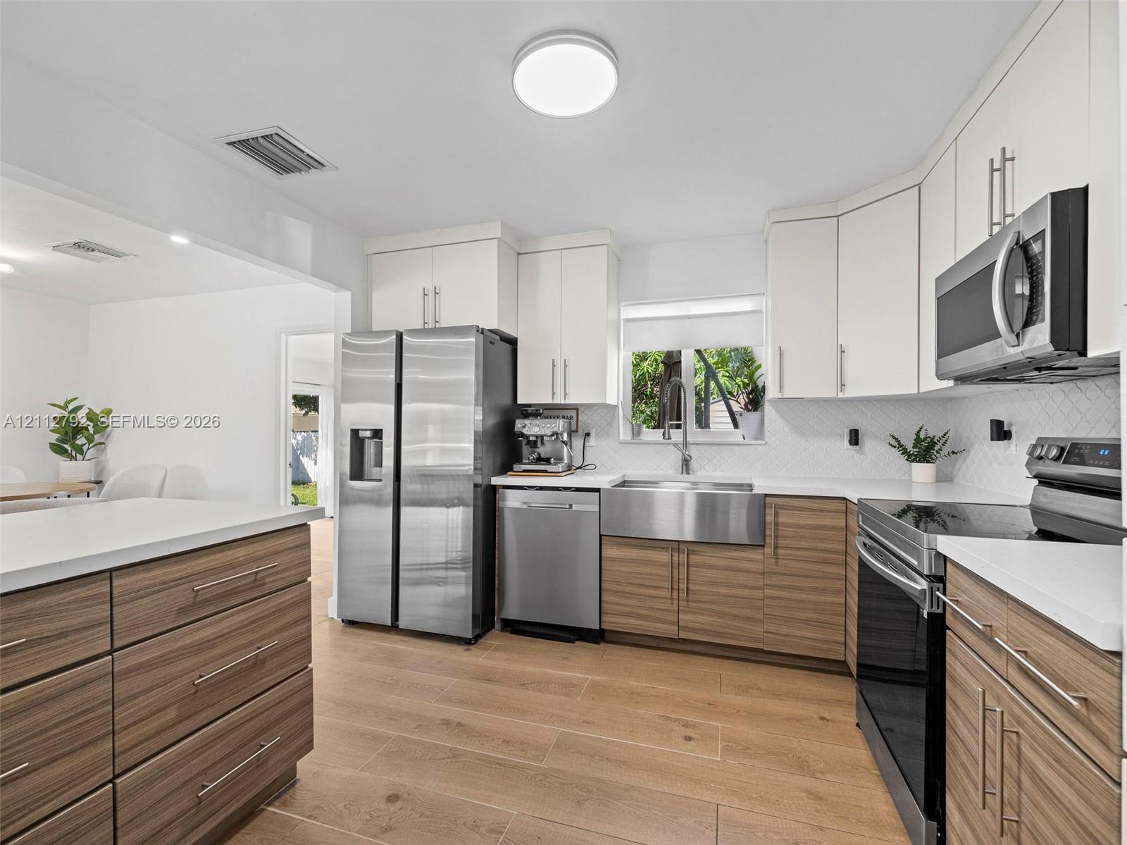 Kitchen featuring two-tone flat-panel cabinetry, stainless steel apron-front sink, quartz countertops, chevron-pattern tile backsplash, and wood-finish flooring