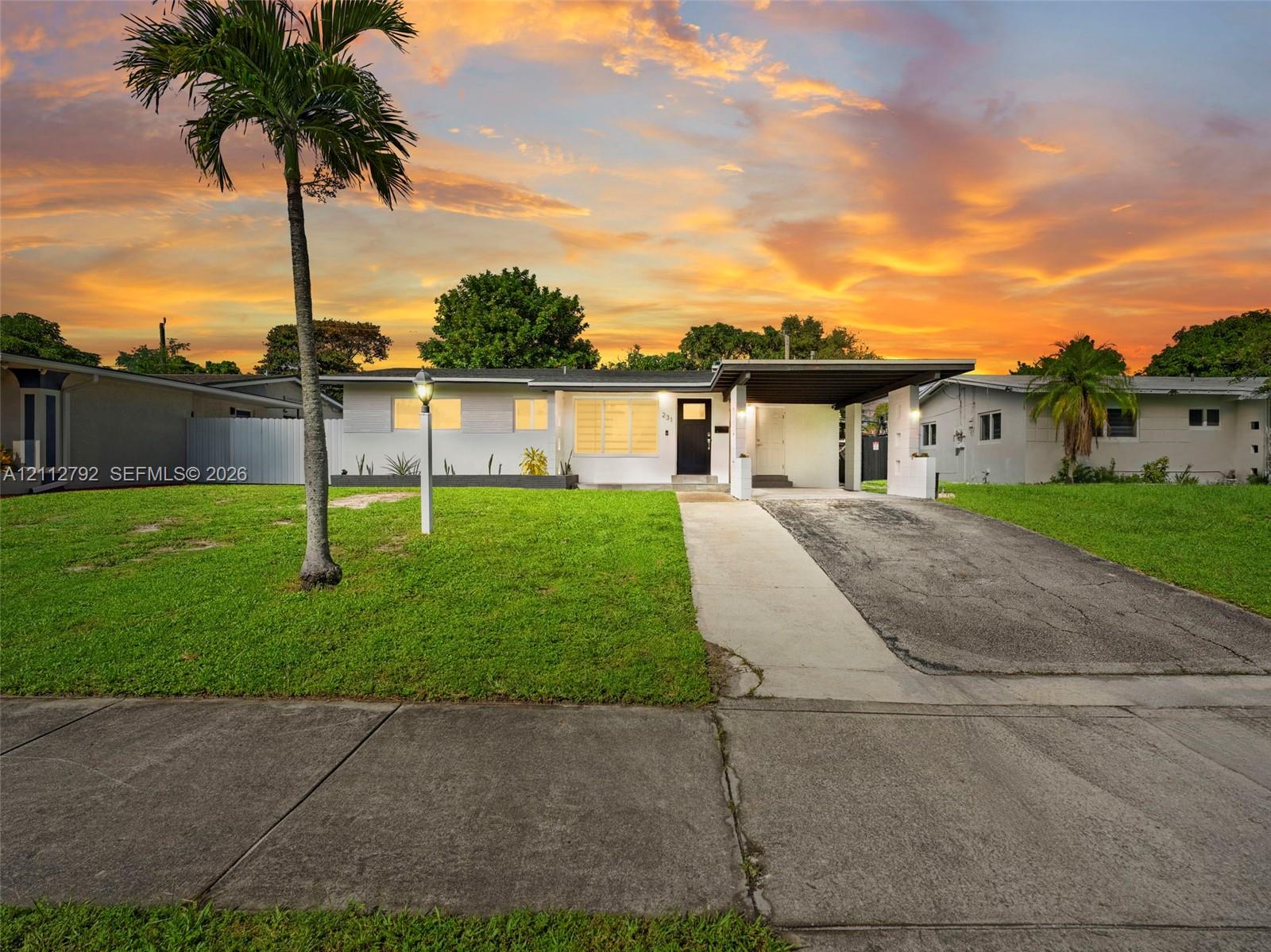 Single-story exterior featuring a painted masonry facade, an integrated carport, a concrete driveway, and mature palm landscaping Single-story exterior featuring a painted masonry facade, an integrated carport, a concrete driveway, and mature palm landscaping